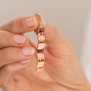 Copper wave earring held between fingers to show its size